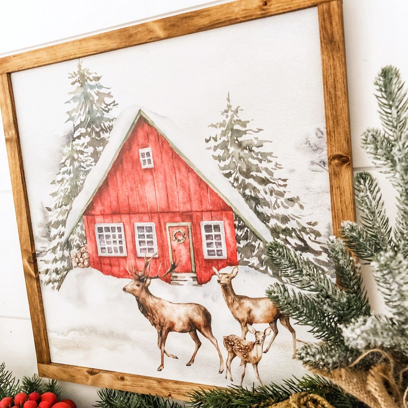 May include: A watercolor painting of a red cabin in a snowy forest with three deer. The cabin has a wreath on the door and snow on the roof. The deer are brown and white and are standing in the snow.