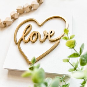 May include: A white wooden sign with a gold heart cutout and the word "love" written in a cursive font inside the heart.
