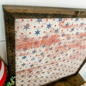 May include: A framed wood sign with a distressed American flag design. The flag is white with red and blue stars and red dots.