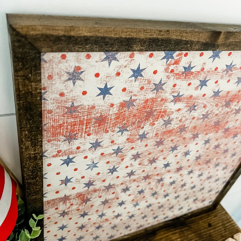 May include: A framed wood sign with a distressed American flag design. The flag is white with red and blue stars and red dots.