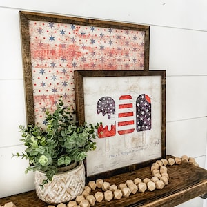 May include: Two framed prints with a patriotic theme. The larger print features a red, white, and blue stars and stripes pattern. The smaller print features three ice cream pops with a red, white, and blue stars and stripes pattern. The text "Stars & Stripes Forever" is printed below the ice cream pops.