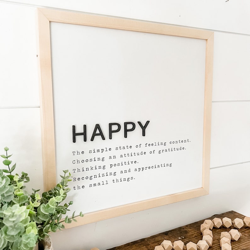 May include: A framed print with the word "HAPPY" in large black letters. The print defines happiness as "The simple state of feeling content. Choosing an attitude of gratitude. Thinking positive. Recognizing and appreciating the small things."
