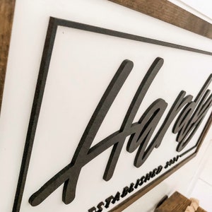 May include: A black wooden sign with the word "Hardy" written in a stylized font. The sign is framed in a dark wood frame and has the text "Established 2021" below the word "Hardy".