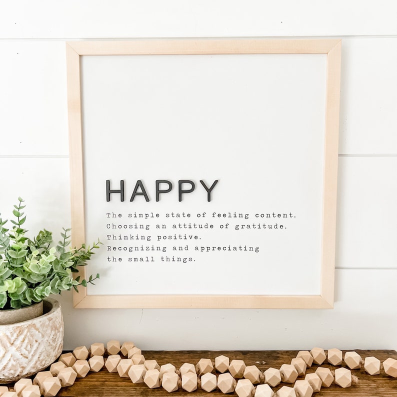 May include: A framed print with the word "HAPPY" in large black letters. The definition of happy is written in black text below the word. The definition is: "The simple state of feeling content. Choosing an attitude of gratitude. Thinking positive. Recognizing and appreciating the small things."