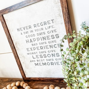 May include: A framed print with a white background and black text that reads "Never regret a day in your life. Good days give happiness. Bad days give experience. Worst days give lessons. And best days give memories."