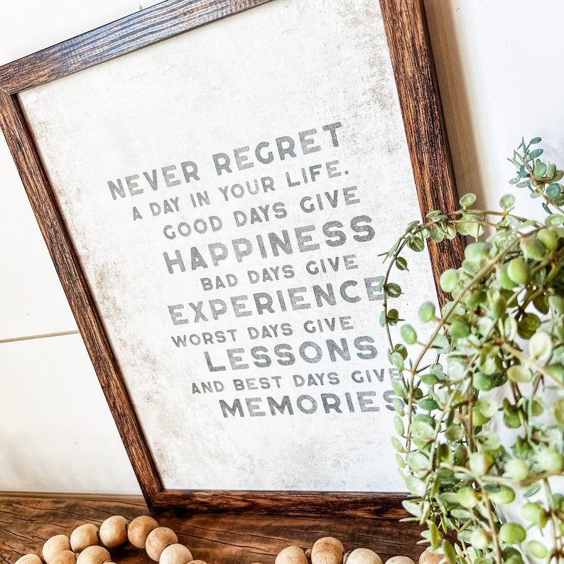 May include: A framed print with a white background and black text that reads "Never regret a day in your life. Good days give happiness. Bad days give experience. Worst days give lessons. And best days give memories."