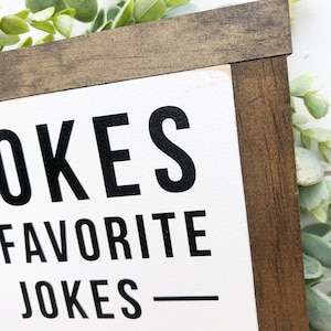 Puede incluir: Un letrero de madera blanco con texto negro que dice "OKES FAVORITE JOKES" con una l&iacute;nea negra debajo del texto.