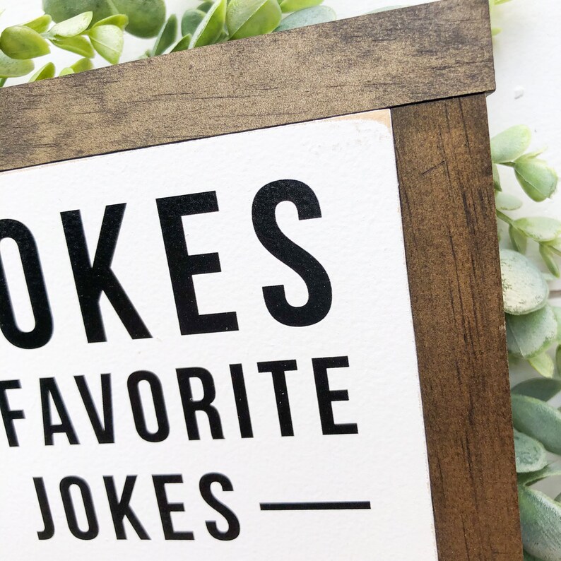 Puede incluir: Un letrero de madera blanco con texto negro que dice "OKES FAVORITE JOKES" con una l&iacute;nea negra debajo del texto.