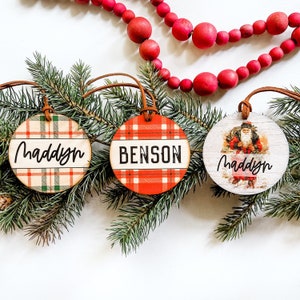 May include: Three round Christmas ornaments with red and green plaid designs and the names "Maddy", "Benson", and "Maddy" written on them.