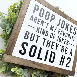 Puede incluir: Un letrero de madera blanco con marco de madera marr&oacute;n. El letrero tiene texto negro que dice "Poop jokes aren't my favorite kind of jokes - but they're a solid #2".