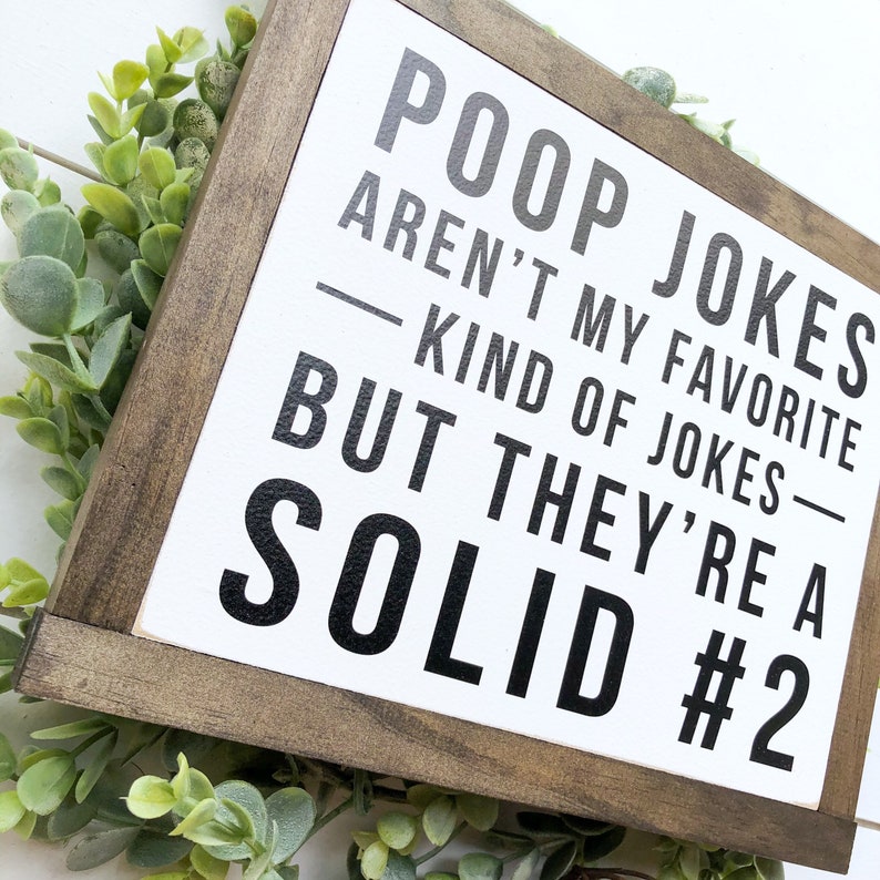 Puede incluir: Un letrero de madera blanco con marco de madera marr&oacute;n. El letrero tiene texto negro que dice "Poop jokes aren't my favorite kind of jokes - but they're a solid #2".