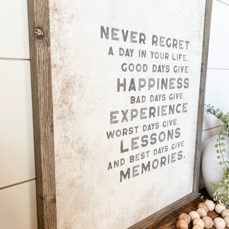 May include: A framed inspirational quote on a white background with a distressed texture. The quote reads: "Never regret a day in your life. Good days give happiness. Bad days give experience. Worst days give lessons. And best days give memories."
