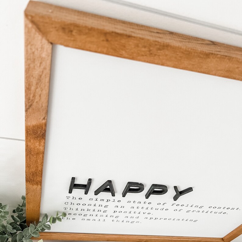 May include: A framed print with the word "HAPPY" in large black letters. The print defines happiness as "the simple state of feeling content. Choosing an attitude of gratitude. Thinking positive. Recognizing and appreciating the small things."