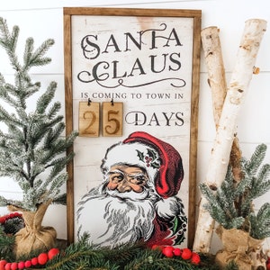 May include: A wooden sign with a vintage illustration of Santa Claus. The sign reads "Santa Claus is coming to town in 25 days".