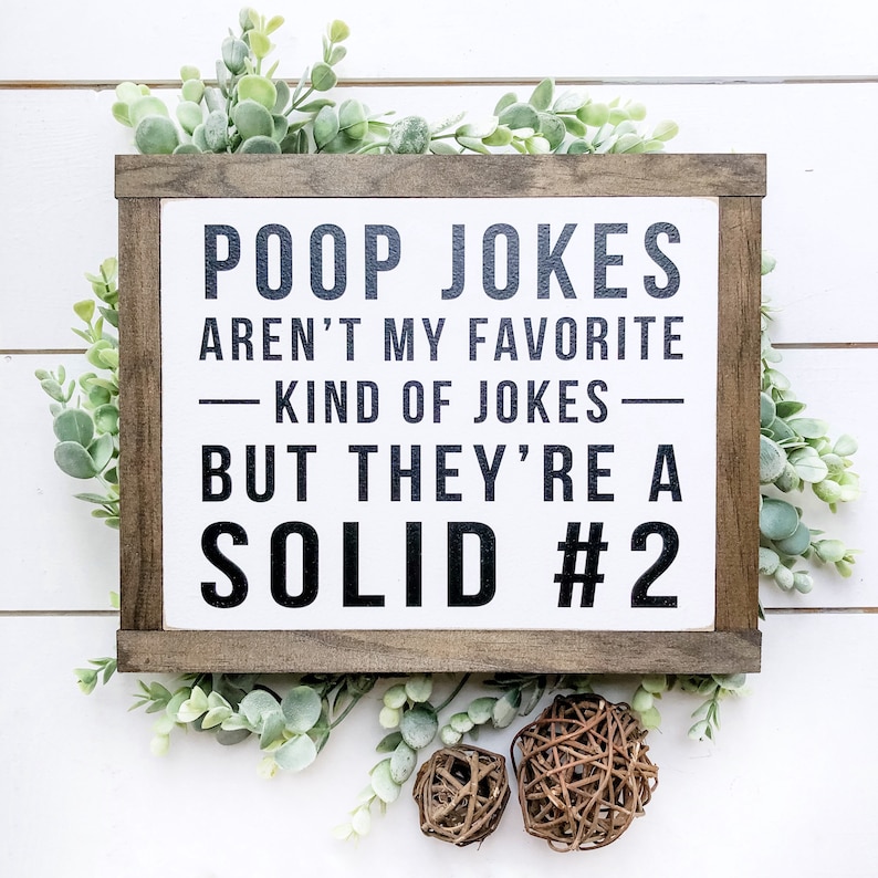 Puede incluir: Un letrero de madera con fondo blanco y texto negro que dice "Poop Jokes Aren't My Favorite Kind of Jokes - But They're A Solid #2".