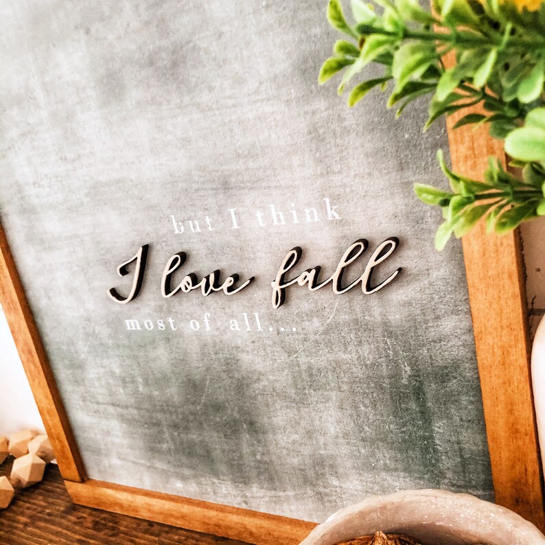 May include: A framed chalkboard sign with the text "but I think I love fall most of all..." in white lettering. The word "fall" is written in a decorative wooden font.