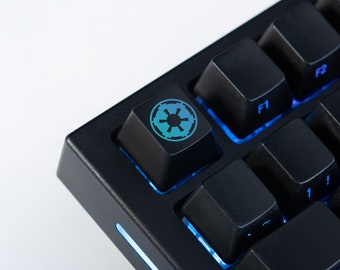 May include: Close-up of a black mechanical keyboard with blue backlighting. The keycap features a teal and blue Imperial symbol. Other keys are visible, including F1, F2, and Tab.