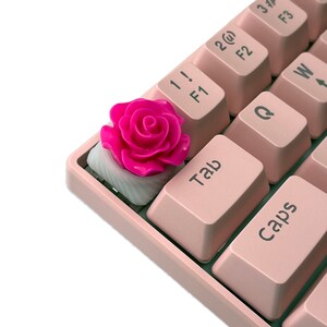 Pu&ograve; includere: Un copritasto rosa a forma di rosa per una tastiera meccanica. Il copritasto &egrave; in plastica e ha una finitura lucida. Il copritasto &egrave; su una tastiera rosa con lettere bianche.