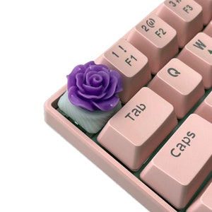 Pu&ograve; includere: Un keycap a forma di rosa viola per una tastiera meccanica. Il keycap &egrave; realizzato in resina e ha una base bianca.