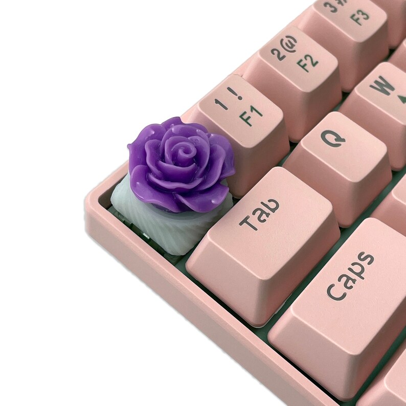 Pu&ograve; includere: Un keycap a forma di rosa viola per una tastiera meccanica. Il keycap &egrave; realizzato in resina e ha una base bianca.