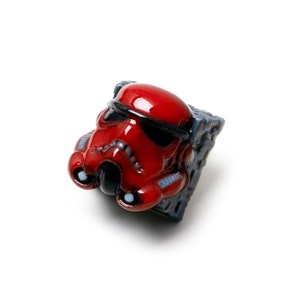 Op de afbeelding: Een rode en zwarte Star Wars Stormtrooper-toetsenkap met een gedetailleerd ontwerp. De toetsenkap is gemaakt van keramiek en heeft een glanzende afwerking.