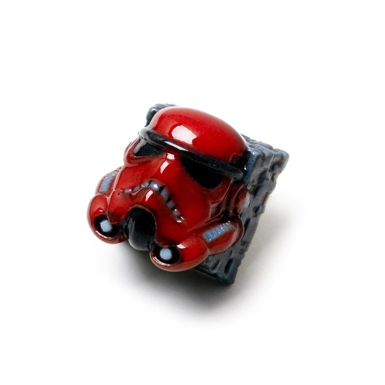 Op de afbeelding: Een rode en zwarte Star Wars Stormtrooper-toetsenkap met een gedetailleerd ontwerp. De toetsenkap is gemaakt van keramiek en heeft een glanzende afwerking.