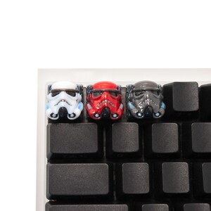 Op de afbeelding: Drie Star Wars-personage toetsencaps in wit, rood en zwart. De toetsencaps bevinden zich op een zwart toetsenbord.