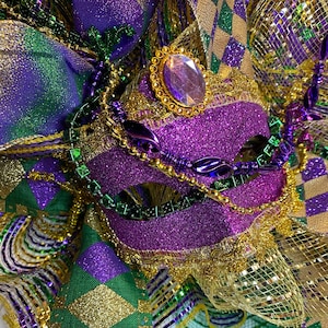May include: Purple and gold Mardi Gras mask with green and gold beads. The mask is decorated with glitter and sequins.