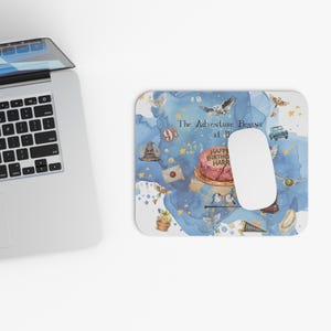 May include: A rectangular mousepad with a watercolor design featuring a cake, owl, and other elements. The text "The Adventure Begins at 11" and "Happy Birthday Harry" are visible. A white computer mouse rests on the pad.