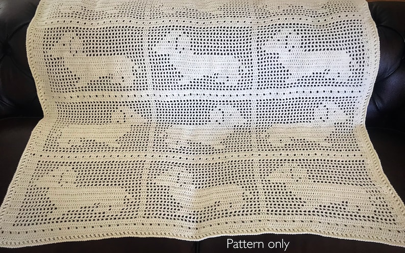 Op de afbeelding: Een gehaakt deken met een delicaat patroon in cr&egrave;mekleur. Het deken ligt op een bruine leren bank. De tekst "Pattern only" is zichtbaar onderaan de afbeelding.