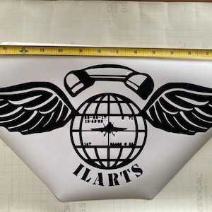 以下が含まれることがあります： 黒と白の電話に翼と地球儀が描かれたステッカー。地球儀の中にはジェット機があり、地球儀の下には「ILARTS」という文字が書かれている。