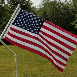 May include: The flag of the United States of America features a blue canton with fifty white stars and thirteen alternating horizontal red and white stripes. The flag is attached to a white pole structure consisting of a vertical and angled arm.