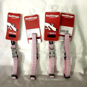 May include: Four Red Dingo pet collars with matching tags. The collars are pink with a gray chevron pattern. Each collar has a gray plastic buckle and a black adjustable strap. The tags are red with a white dog graphic and the word "Reflective".