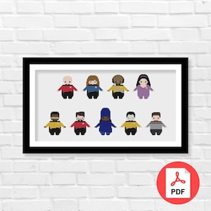 May include: A framed cross-stitch print depicting eleven figures in uniform. The figures are in various colours, with different hairstyles and skin tones. The print is in a black frame and set against a white background.