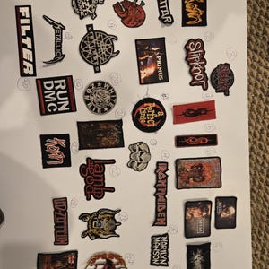 May include: A collection of embroidered music band patches featuring various logos and graphic designs, including names like Ozzy Osbourne, Metallica, Filter, Korn, Slipknot, Primus, A Perfect Circle, Slayer, Lamb of God, Iron Maiden, and Marilyn Manson.