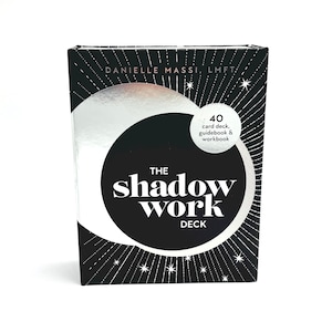 May include: A black and white card deck box with the text "THE shadow work DECK". The box also includes the text "DANIELLE MASSI, LMFT" and "40 card deck, guidebook & workbook". The box has a silver circle in the center.