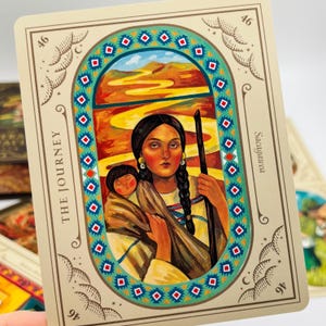 May include: A tarot card featuring an illustration of a woman holding a child, with a staff. The card is framed with a decorative border and the words "THE JOURNEY" and "Sacagawea". The background depicts a landscape with a winding path.