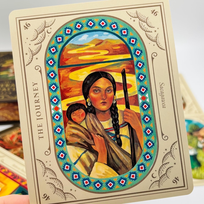 May include: A tarot card featuring an illustration of a woman holding a child, with a staff. The card is framed with a decorative border and the words "THE JOURNEY" and "Sacagawea". The background depicts a landscape with a winding path.