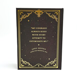 May include: A hardcover book with a black cover and gold decorative accents. The cover features a quote by Jane Austen from Pride and Prejudice. The quote reads, "My courage always rises with every attempt to intimidate me."