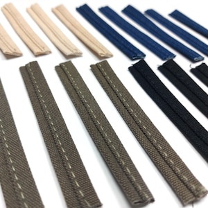 May include: Assortment of different colored fabric trims, including beige, gray, blue, and black. The trims are all flat and have a stitched edge.