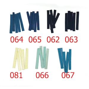 Puede incluir: Una colección de tiras de tela en varios colores, incluyendo tonos de azul, negro y crema. Cada grupo de tiras está etiquetado con un número en rojo. Las tiras parecen tener textura y están dispuestas sobre un fondo blanco.