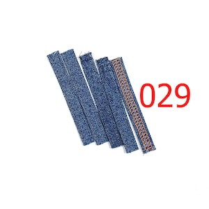 Może przedstawiać: Zbliżenie kilku niebieskich pasków materiału dżinsowego z widocznym splotem. Jeden pasek ma brązowy ścieg owerlokowy. Numer "029" jest wydrukowany na czerwono. Idealny do projektów krawieckich i rzemieślniczych.