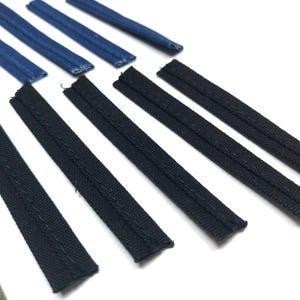 Puede incluir: Primer plano de una cinta de adorno de tela negra y azul. La cinta está doblada y dispuesta en filas sobre una superficie blanca.