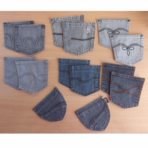 May include: A collection of denim jean pockets in shades of blue and grey, displayed on a light brown surface. The pockets showcase diverse stitching patterns and designs, highlighting various styles and washes.