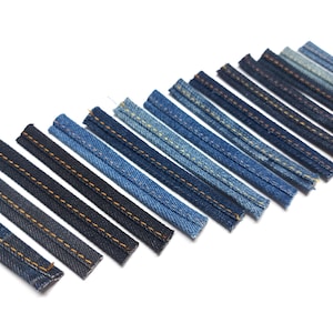 Może przedstawiać: Asortyment pasków materiału dżinsowego w różnych odcieniach niebieskiego, ułożonych po przekątnej na białym tle. Każdy prostokątny pasek ma widoczne szwy z kontrastującą pomarańczowo-żółtą nicią, sugerując motyw szycia lub rękodzieła.