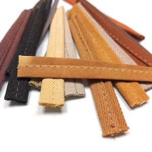 May include: Assortment of brown, beige, and tan fabric trim with a stitched edge. The trim is arranged in a fan shape.