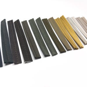 May include: A collection of 15 fabric trim samples in various shades of gray, green, and beige. The trim is woven with a subtle stitch detail.
