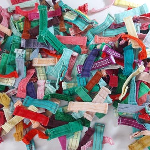 May include: A collection of colorful fabric scraps in various shapes and sizes. The scraps are in shades of red, green, blue, pink, and yellow. Some pieces have textured patterns and stitching details, creating a visually rich assortment.