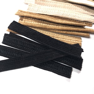 Puede incluir: Un surtido de bandas elásticas en varios colores. La imagen muestra varias bandas elásticas negras, beige y crema. Las bandas son rectangulares y parecen estar hechas de un material tejido. Las bandas probablemente se utilizan para proyectos de costura o manualidades.