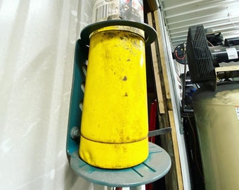 May include: A yellow propane tank with a black torch attached is mounted on a blue metal bracket. The tank is labeled "MAP/Pro Premium Torch Fuel".